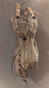 SINGE-D, art piece by janell mithani of a miniature dress made from upcycled tea bags with burnt hem and 19 beads to represent the deaths in the Eaton Fire. 
